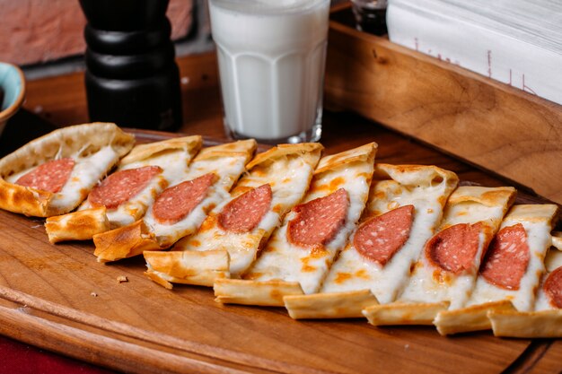 Vista lateral de pide turco con salchichas de salami dispuestas sobre una tabla para cortar madera