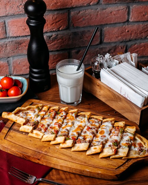 Vista lateral de pide turco con verduras carne y queso dispuestos sobre una tabla para cortar madera