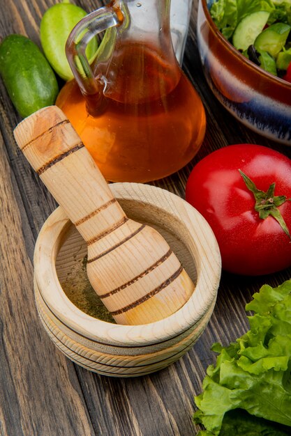 Vista lateral de la pimienta negra en la trituradora de ajo con aceite derretido lechuga tomate pepino sal y ensalada de verduras sobre superficie de madera