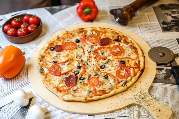 Vista lateral de pizza en una bandeja con tomates y pimientos de colores en un periódico