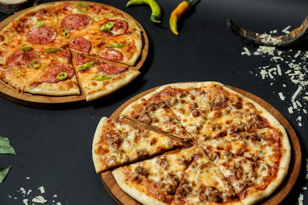 Vista lateral pizza de carne en una bandeja con pizza de salami y pimientos picantes en mesa negra
