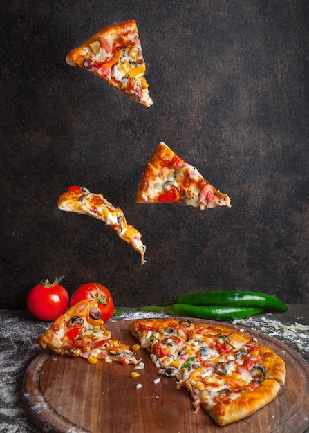 Vista lateral de pizza con pimiento y tomate y rebanadas de pizza en utensilios de cocina