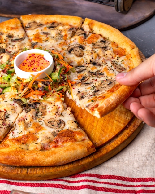 Vista lateral de pizza con pollo y champiñones servidos con salsa y ensalada de verduras en placa de madera