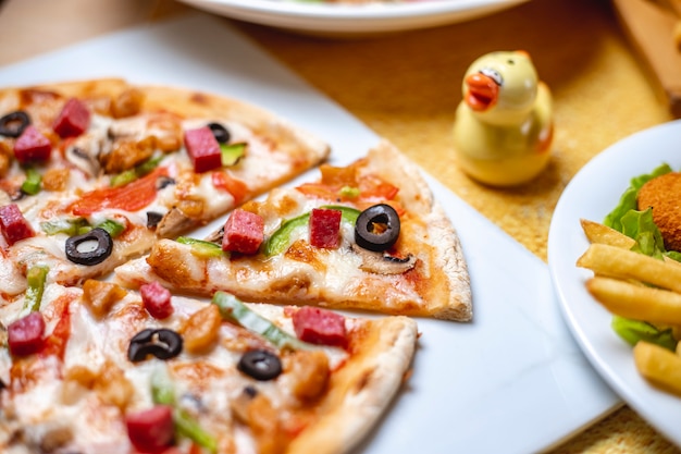 Vista lateral pizza con pollo a la parrilla salami pimiento aceituna negra y queso sobre la mesa