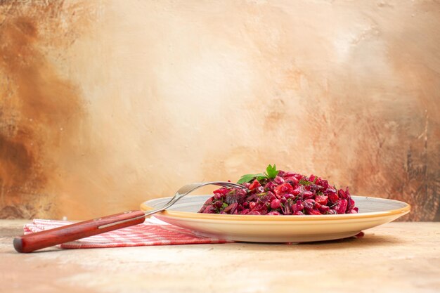 Vista lateral del plato de una ensalada roja con verduras sobre una servilleta marcada y el tenedor sobre un fondo de madera