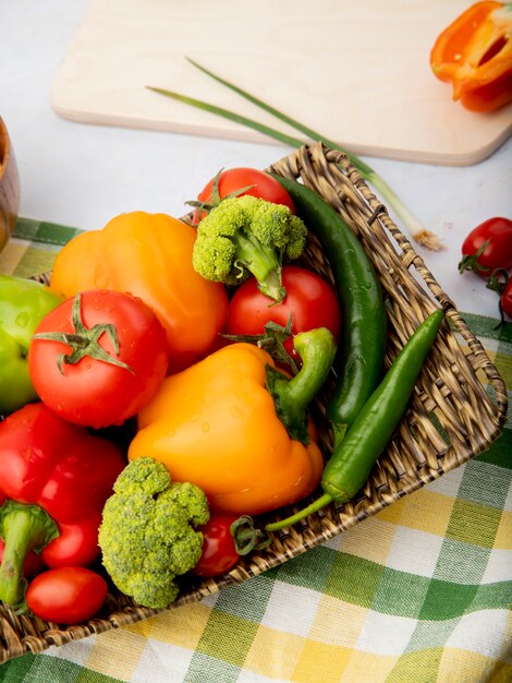 Vista lateral del plato lleno de verduras como pimientos tomates brócoli sobre tela escocesa sobre superficie blanca