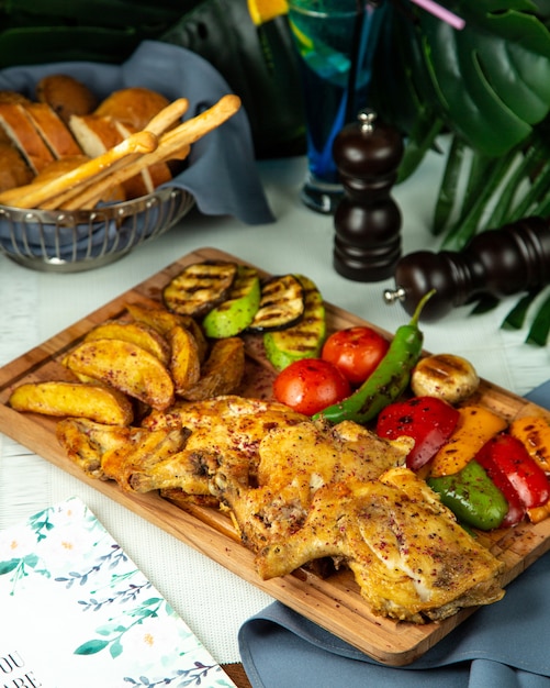 Vista lateral pollo al tabaco frito con papas y verduras a la parrilla sobre una tabla de madera