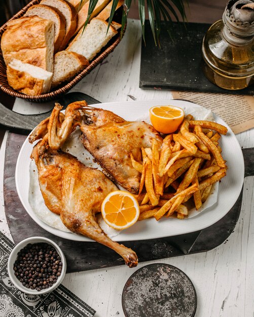 Vista lateral de pollo asado con papas fritas en un plato blanco sobre una tabla para cortar madera