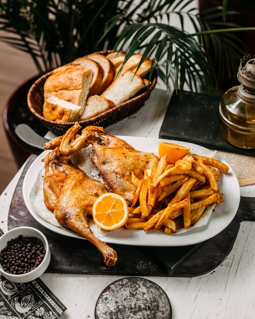 Vista lateral de pollo asado con papas fritas en un plato blanco sobre una tabla para cortar madera