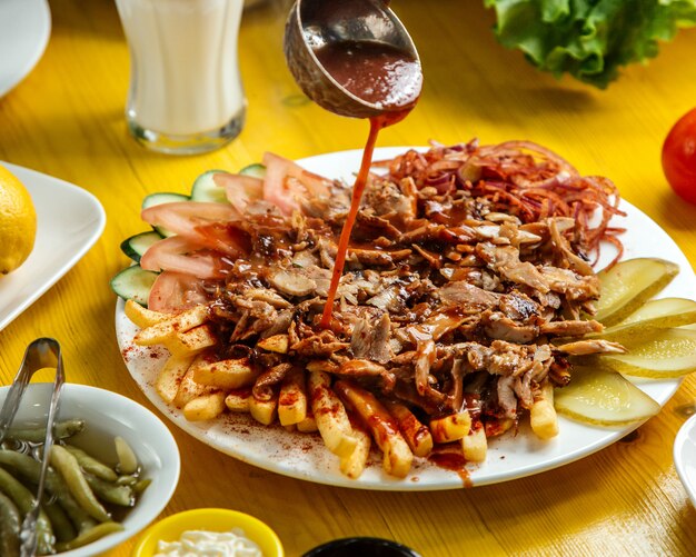 Vista lateral de pollo doner kebab en el plato con pan papas fritas tomates cebolla encurtidos y ensalada