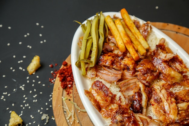 Vista lateral de pollo frito con papas fritas y encurtidos en un plato con especias en una bandeja