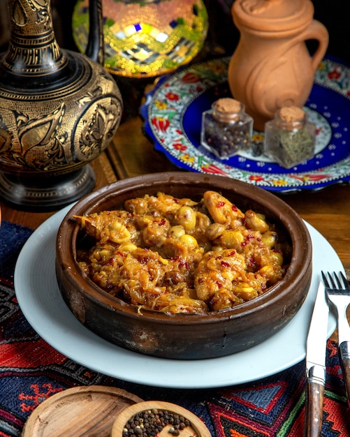 Vista lateral del pollo guisado con castañas y cebolla en un recipiente de arcilla sobre una mesa de madera