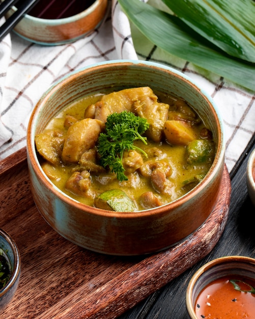 Vista lateral del pollo guisado con verduras en un recipiente de arcilla sobre mantel a cuadros