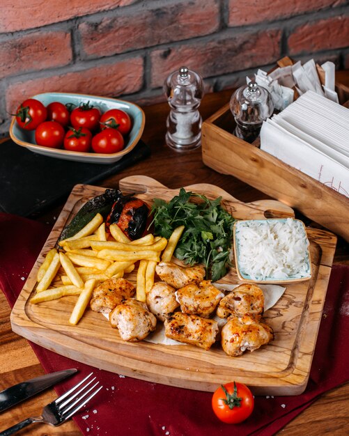 Vista lateral de pollo a la parrilla y carne de verduras con papas fritas en una tabla de madera