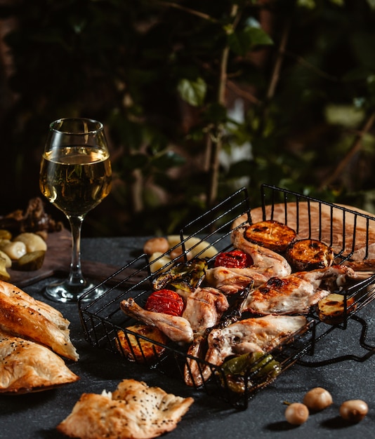 Vista lateral de pollo a la parrilla con verduras y una copa de vino en una mesa negra