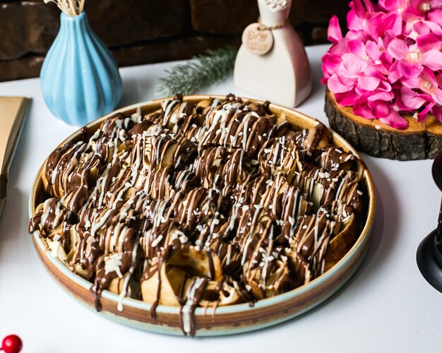 Vista lateral del postre con bollos de masa cubiertos con jarabe de chocolate sobre la mesa