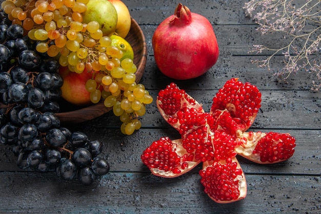 Vista lateral de primer plano frutas en placa placa marrón de uvas blancas y negras limas peras manzanas junto a granada pillada granada roja madura y ramas sobre fondo gris