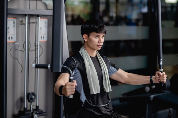 Vista lateral, primer plano retrato joven guapo en ropa deportiva sentado para hacer ejercicio de prensa de pecho de máquina en el gimnasio moderno, mirando hacia adelante,