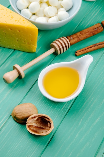 Foto gratuita vista lateral del queso mozzarella con un trozo de queso holandés con miel de nueces y palitos de canela en madera verde