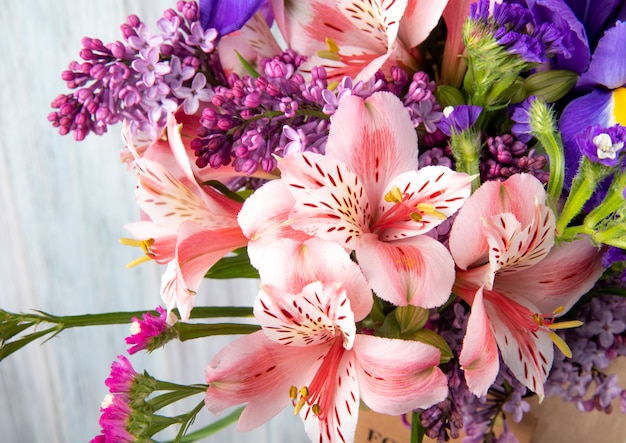 Vista lateral de un ramo de alstroemeria de color rosa y morado lila iris y flores de statice en papel artesanal sobre fondo blanco de madera