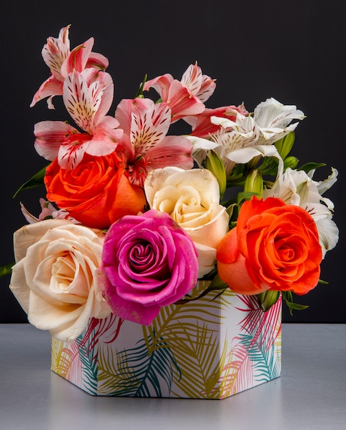 Vista lateral de un ramo de rosas coloridas y flores de alstroemeria de color rosa en una caja de regalo sobre la mesa negra
