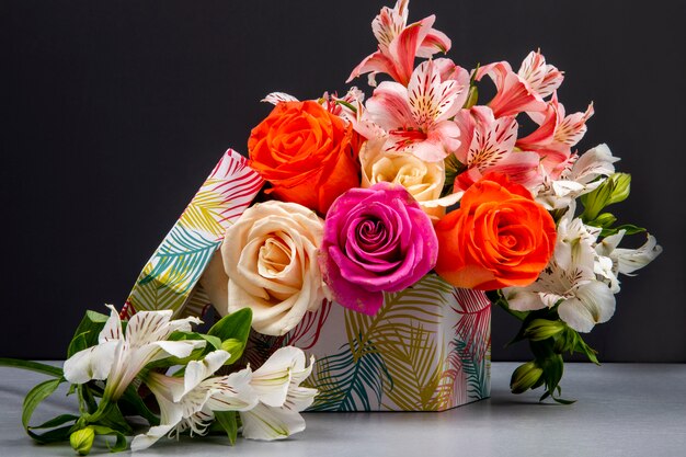 Vista lateral de un ramo de rosas coloridas y flores de alstroemeria de color rosa en una caja de regalo sobre la mesa negra