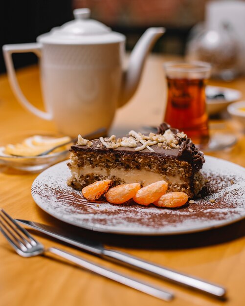 Vista lateral de una rebanada de pastel de chocolate con crema de vainilla y nueces servido con rodajas de mandarina en un plato blanco