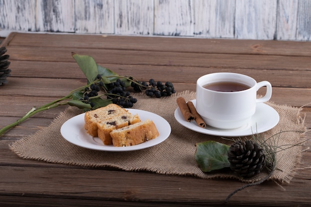 Vista lateral de rebanadas de bizcocho en un plato con una taza de té negro en rústico