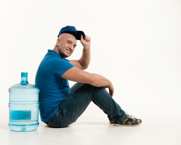 Vista lateral del repartidor con gorra posando con botella de agua