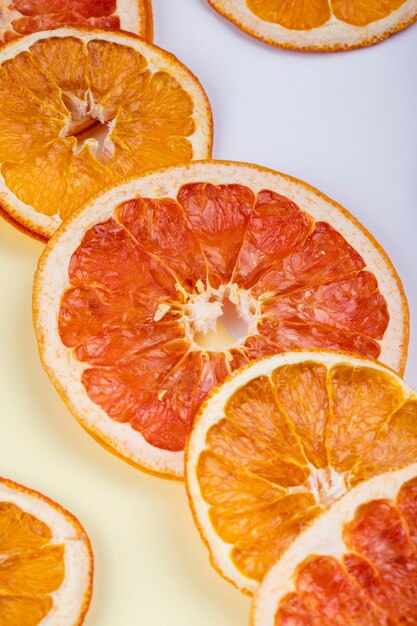 Vista lateral de rodajas secas de naranja y pomelo dispuestas sobre fondo blanco.