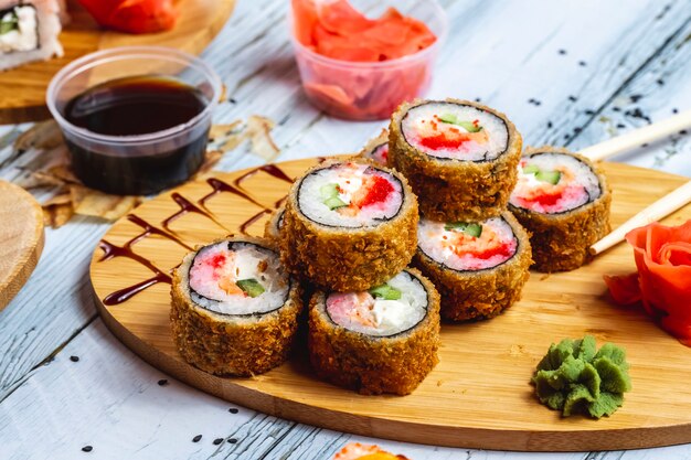 Vista lateral rollo caliente sushi frito con salmón tomate pepino queso crema jengibre wasabi y salsa de soja sobre la mesa