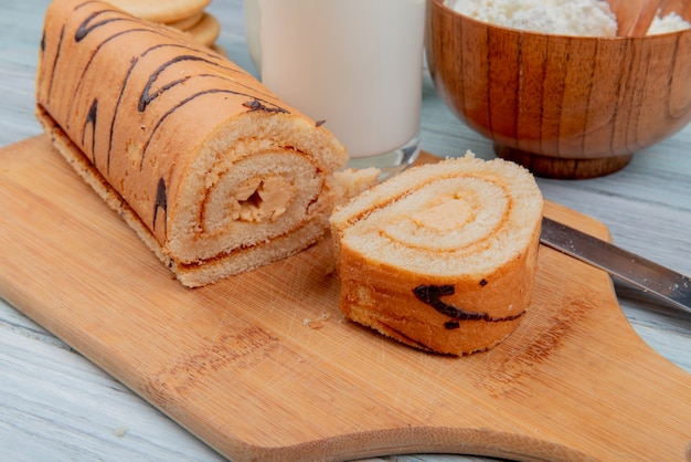 Foto gratuita vista lateral del rollo cortado y rebanada con cuchillo en la tabla de cortar y galletas de requesón de leche en la mesa de madera