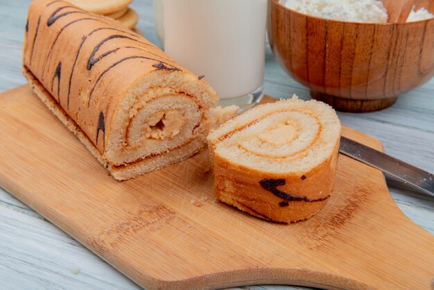 Vista lateral del rollo cortado y rebanada con cuchillo en la tabla de cortar y galletas de requesón de leche en la mesa de madera