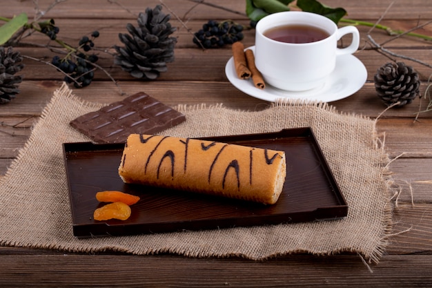 Foto gratuita vista lateral del rollo suizo con mermelada de albaricoque servido con una taza de té en rústico