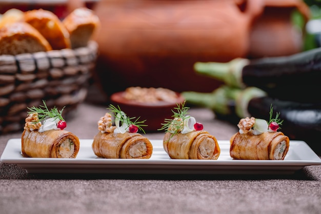 Vista lateral de rollos de berenjenas fritas con nueces y ajo decoradas con eneldo sobre la mesa