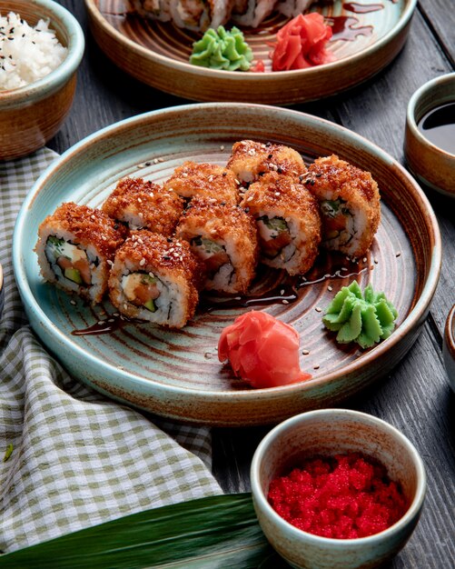 Vista lateral de rollos de sushi fritos calientes con aguacate de salmón y queso servido con jengibre y wasabi en un plato sobre madera