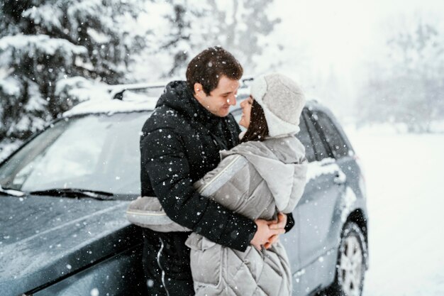 Vista lateral de la romántica pareja besándose en la nieve durante un viaje por carretera