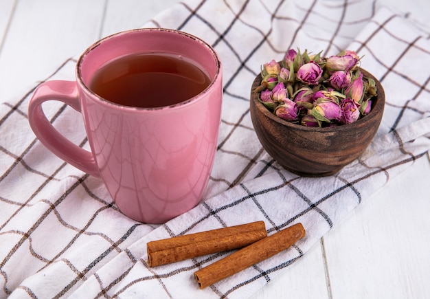 Vista lateral rosa taza de té con canela y flores secas sobre una toalla blanca a cuadros