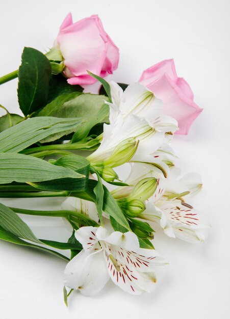 Vista lateral de rosas de color rosa y blanco y flores de alstroemeria sobre fondo blanco.