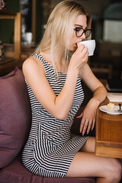 Vista lateral de la rubia joven bebiendo café en la cafetería