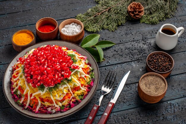 Vista lateral sabrosa comida apetitosa comida navideña y cuencos de aceite y especias junto a las ramas de abeto tenedor cuchillo con conos