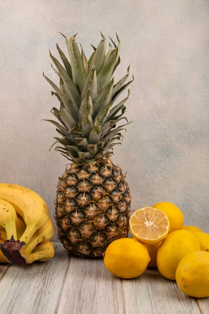 Vista lateral de sabrosas frutas como plátanos, piña y limones aislados sobre una superficie gris