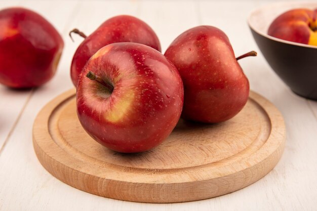 Vista lateral de sabrosas manzanas rojas sobre una placa de cocina de madera sobre una superficie de madera blanca
