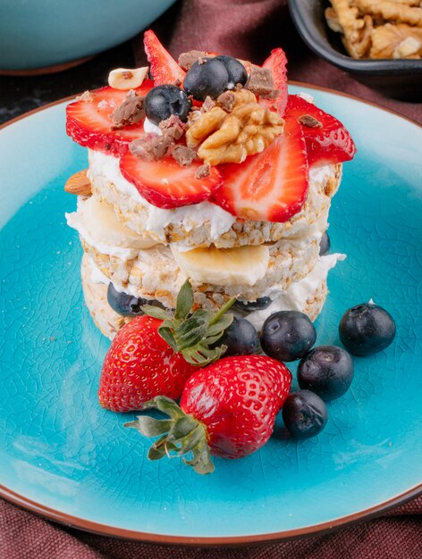 Vista lateral de sabroso pan crujiente con arándanos maduros, fresas y nueces con crema agria en un plato de cerámica