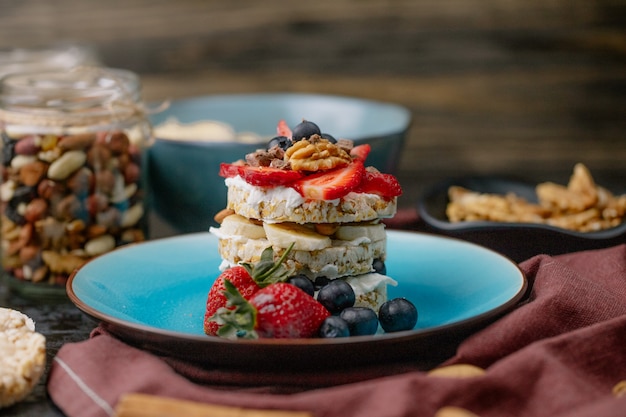 Foto gratuita vista lateral de sabroso pan crujiente con arándanos maduros, fresas y nueces con crema agria en un plato de cerámica