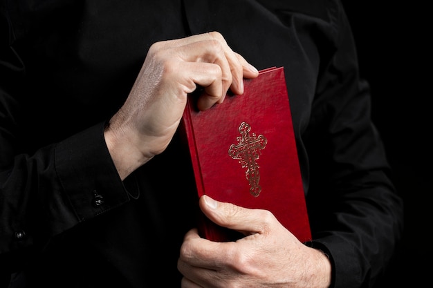 Vista lateral sacerdote sosteniendo biblia con tapa roja