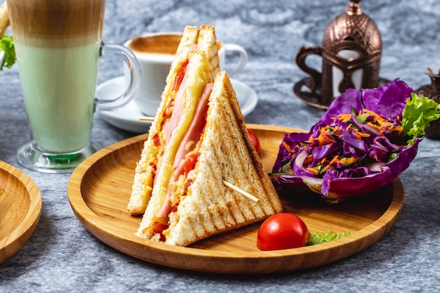 Vista lateral sandwich de jamón y queso con tomate verde zanahoria y col roja en un tablero