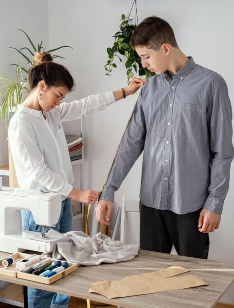 Vista lateral del sastre femenino midiendo la camisa de los clientes masculinos