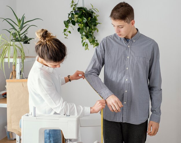 Vista lateral del sastre femenino midiendo la camisa de los clientes masculinos