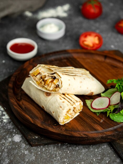 Vista lateral del shaurma kebab sobre tabla de madera con salsas en negro